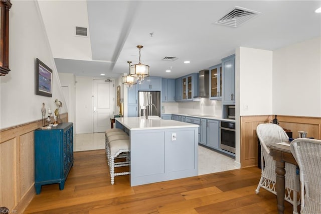 kitchen featuring glass insert cabinets, stainless steel appliances, a center island with sink, and visible vents