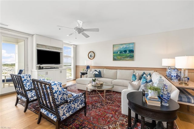 living room with light wood-style floors, a ceiling fan, a wealth of natural light, and wainscoting