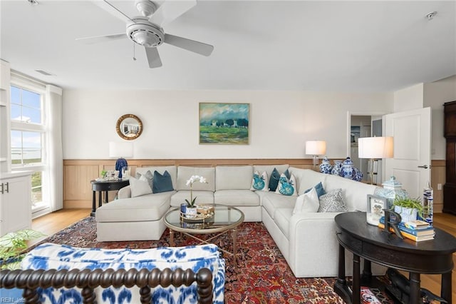 living area with a wainscoted wall, ceiling fan, light wood finished floors, and visible vents