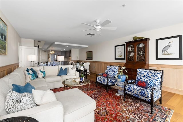 living area featuring ceiling fan with notable chandelier, visible vents, wood finished floors, and wainscoting