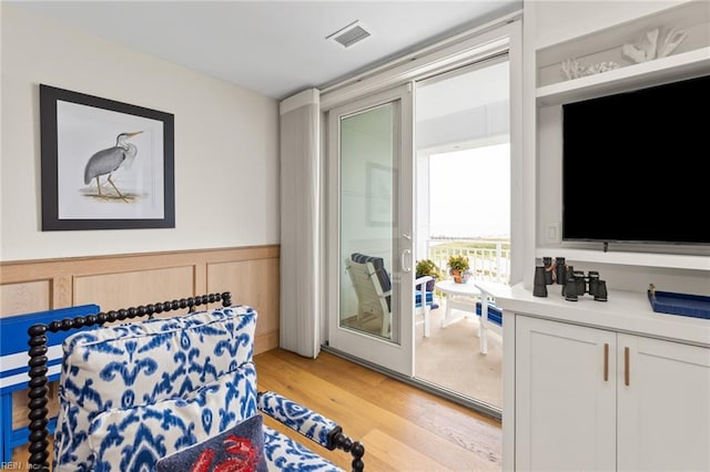 bedroom with light wood-type flooring, wainscoting, and visible vents