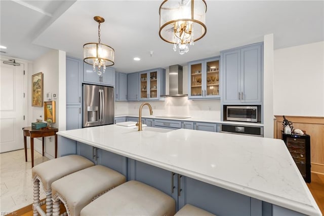 kitchen featuring appliances with stainless steel finishes, glass insert cabinets, hanging light fixtures, wall chimney range hood, and a sink