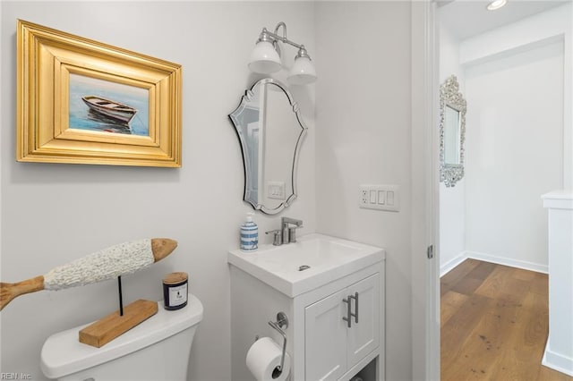 half bath with toilet, baseboards, wood finished floors, and vanity