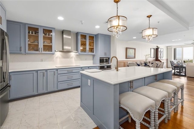 kitchen featuring decorative light fixtures, open floor plan, light countertops, wall chimney range hood, and glass insert cabinets