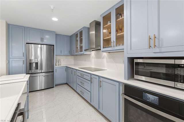 kitchen with glass insert cabinets, appliances with stainless steel finishes, marble finish floor, light countertops, and wall chimney range hood