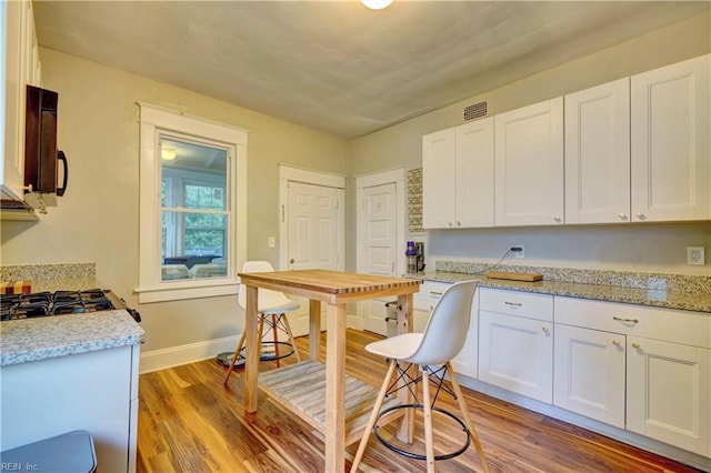 kitchen with black microwave, visible vents, light stone countertops, light wood-type flooring, and white cabinetry