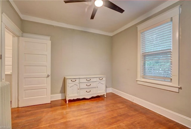 empty room featuring a ceiling fan, baseboards, crown molding, and light wood finished floors