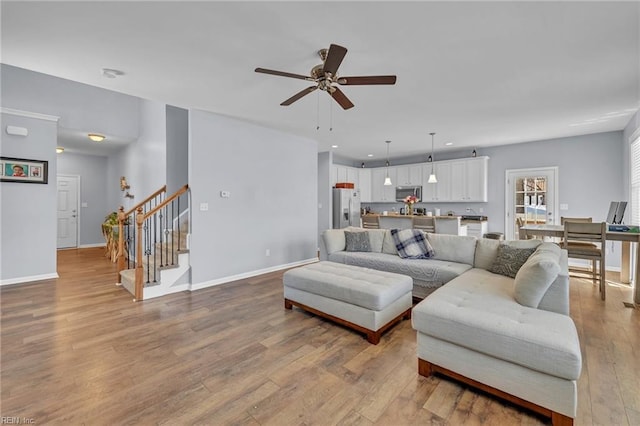 living area with light wood-style flooring, ceiling fan, stairway, and baseboards