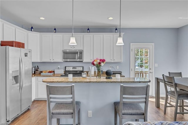 kitchen featuring appliances with stainless steel finishes, a kitchen bar, a center island with sink, and pendant lighting