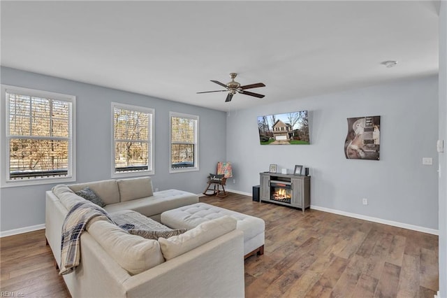 living area featuring ceiling fan, a fireplace, wood finished floors, and baseboards