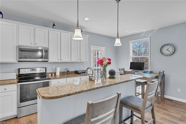 kitchen featuring appliances with stainless steel finishes, pendant lighting, white cabinetry, and a center island with sink