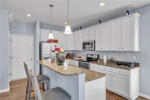 kitchen with white cabinets, a kitchen island, appliances with stainless steel finishes, hanging light fixtures, and light stone countertops