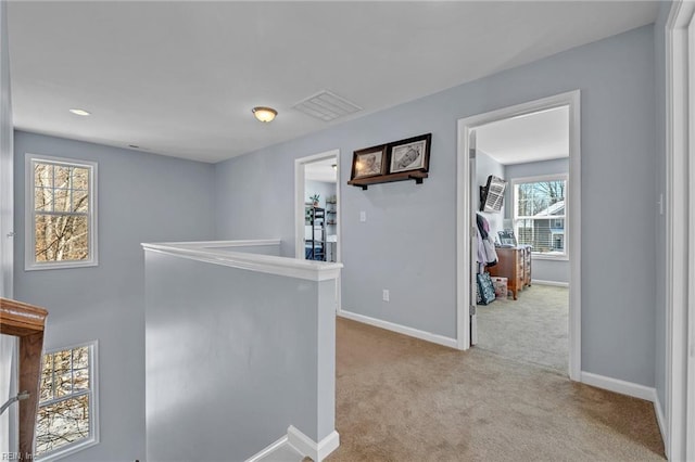 hallway featuring baseboards, light colored carpet, visible vents, and an upstairs landing