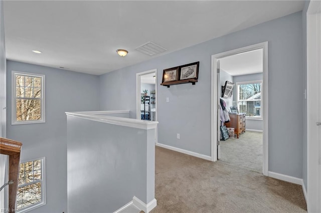 hall with baseboards, light carpet, visible vents, and an upstairs landing