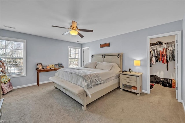 bedroom featuring a walk in closet, light colored carpet, and baseboards