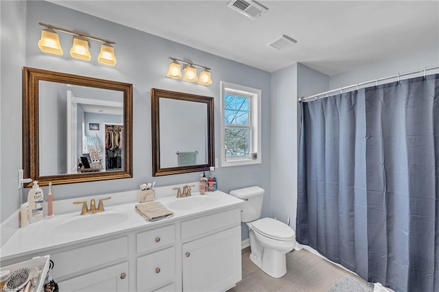 bathroom with visible vents, a sink, toilet, and double vanity