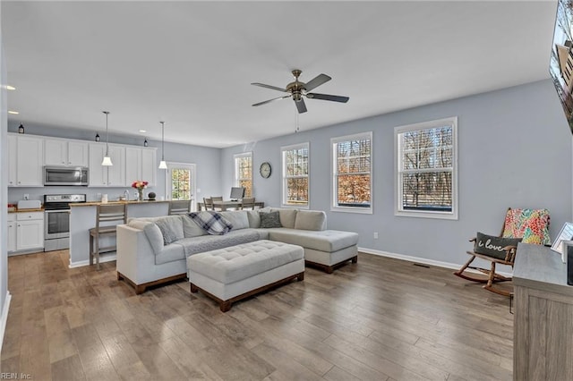 living area with a ceiling fan, baseboards, and wood finished floors