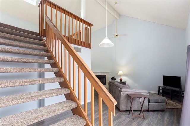 stairway with high vaulted ceiling, a tile fireplace, wood finished floors, visible vents, and beamed ceiling