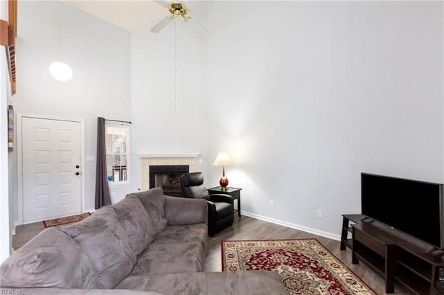 living room featuring a fireplace, a high ceiling, a ceiling fan, wood finished floors, and baseboards