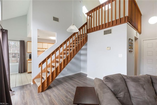 staircase featuring high vaulted ceiling, wood finished floors, and visible vents