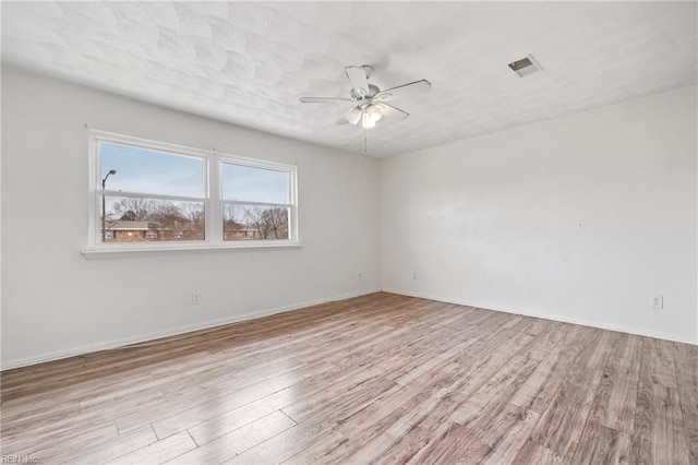 spare room featuring light wood-style floors, visible vents, baseboards, and a ceiling fan