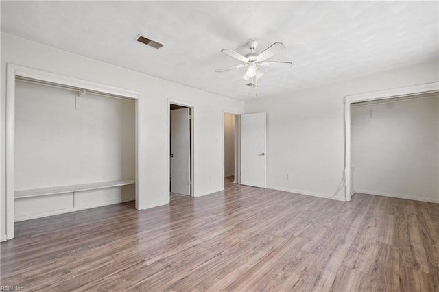 unfurnished bedroom featuring visible vents, ceiling fan, two closets, and wood finished floors