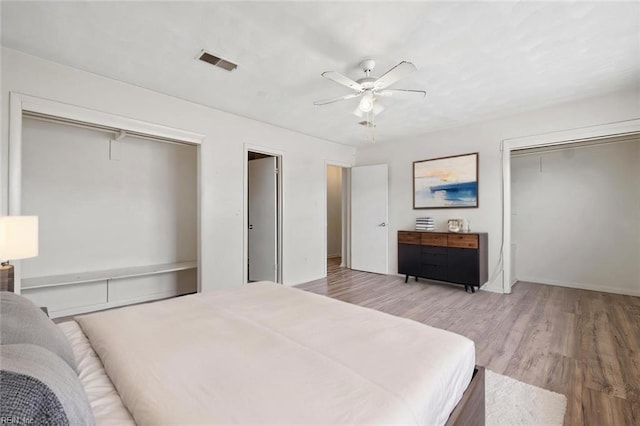 bedroom with a ceiling fan, visible vents, light wood-style flooring, and multiple closets