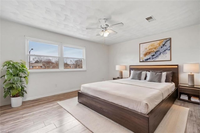 bedroom featuring light wood finished floors, baseboards, visible vents, and ceiling fan