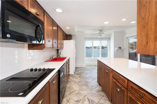 kitchen featuring a water view, a sink, light countertops, black appliances, and backsplash