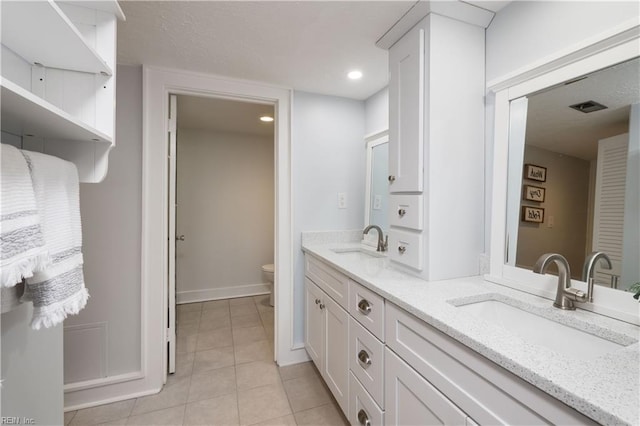 bathroom with toilet, double vanity, a sink, and tile patterned floors