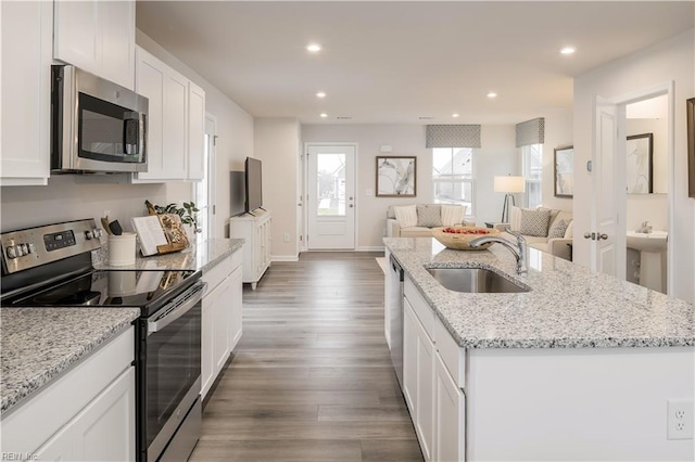 kitchen with a sink, white cabinets, open floor plan, appliances with stainless steel finishes, and an island with sink