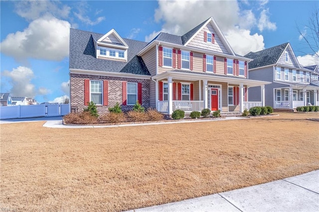 view of front facade featuring a porch, brick siding, a shingled roof, fence, and a front lawn