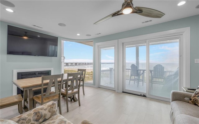 dining space featuring ceiling fan, a fireplace, visible vents, and light wood-style floors