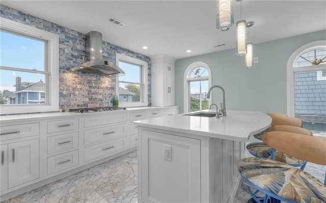 kitchen featuring marble finish floor, stainless steel gas cooktop, visible vents, a sink, and wall chimney exhaust hood