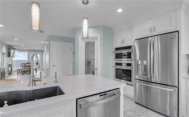 kitchen with light stone counters, a sink, white cabinets, appliances with stainless steel finishes, and decorative light fixtures