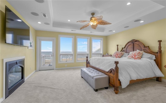 carpeted bedroom featuring access to exterior, a tray ceiling, visible vents, and a glass covered fireplace