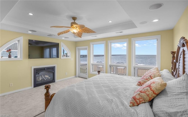 carpeted bedroom with recessed lighting, baseboards, access to outside, a tray ceiling, and a glass covered fireplace