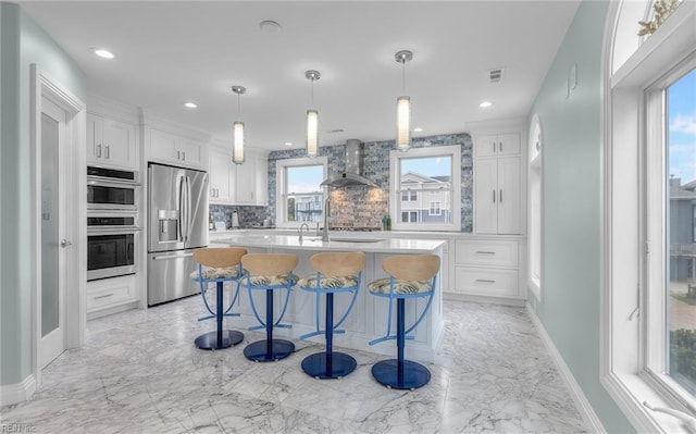 kitchen with marble finish floor, wall chimney exhaust hood, appliances with stainless steel finishes, and white cabinetry