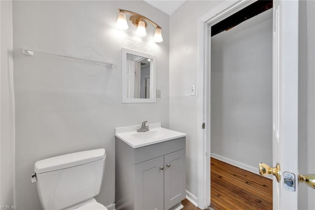 half bath featuring toilet, wood finished floors, vanity, and baseboards