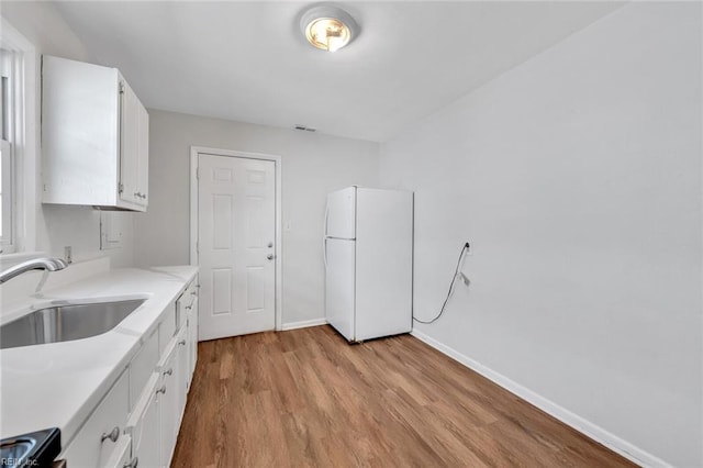 kitchen featuring a sink, white cabinetry, light countertops, light wood-type flooring, and freestanding refrigerator