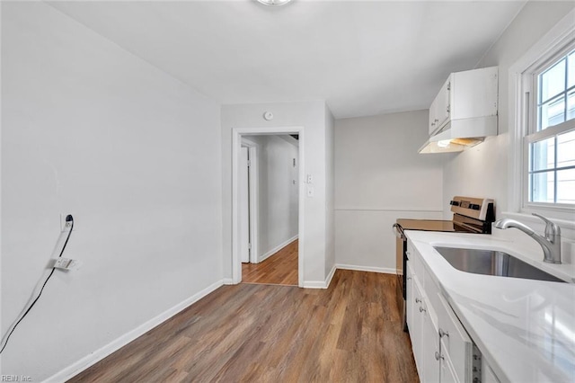 kitchen with a sink, a healthy amount of sunlight, white cabinets, light countertops, and stainless steel electric range oven