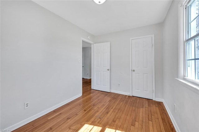 unfurnished bedroom featuring light wood-type flooring, multiple windows, and baseboards