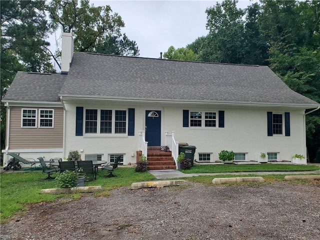 view of front of home featuring brick siding, roof with shingles, a chimney, entry steps, and a front lawn