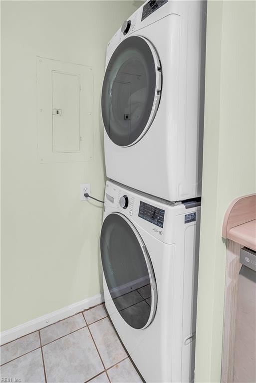 clothes washing area featuring light tile patterned floors, laundry area, baseboards, stacked washing maching and dryer, and electric panel