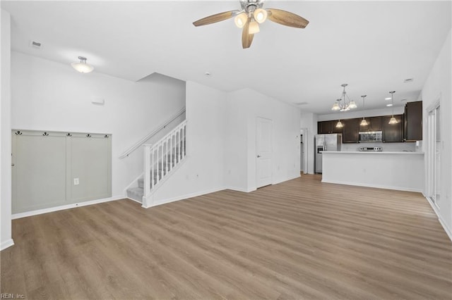 unfurnished living room with light wood-type flooring, stairs, baseboards, and ceiling fan with notable chandelier