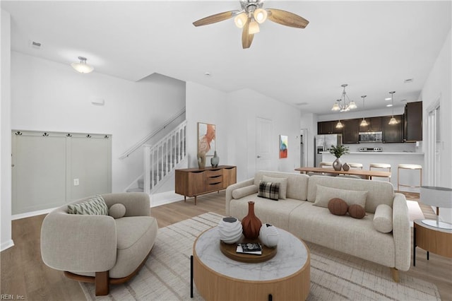 living area featuring ceiling fan with notable chandelier, light wood-type flooring, and stairs