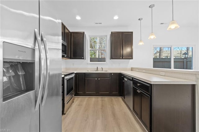 kitchen featuring stainless steel appliances, light countertops, light wood-style floors, pendant lighting, and a sink