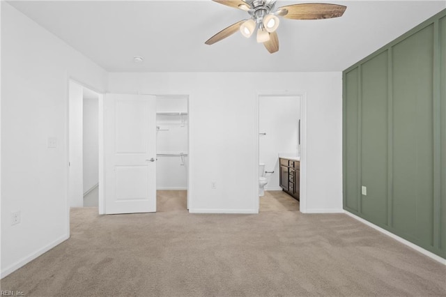 unfurnished bedroom featuring a walk in closet, a closet, light colored carpet, ensuite bathroom, and a ceiling fan