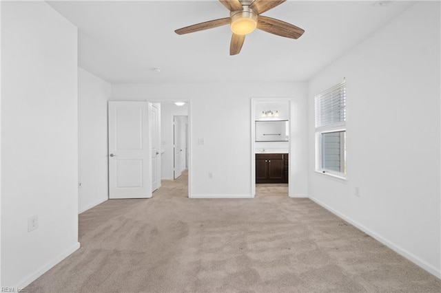 unfurnished bedroom featuring light carpet, ensuite bath, baseboards, and a ceiling fan