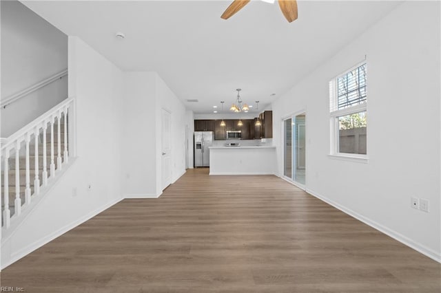 unfurnished living room with recessed lighting, ceiling fan with notable chandelier, wood finished floors, baseboards, and stairway